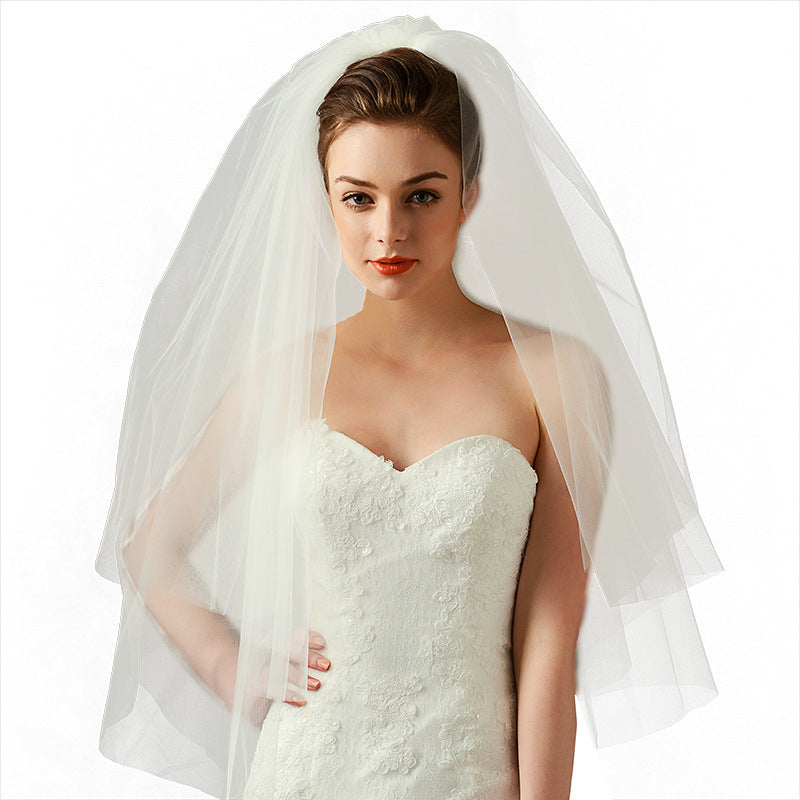 Front view of a bride wearing the Juliette sheer short wedding veil with a romantic bridal gown