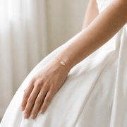 Bride wearing the Margot delicate gold-tone bracelet with an oval centerpiece against an ivory wedding dress