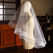 Mannequin displaying the Celeste satin-trim double-layer bridal veil in a warm atelier