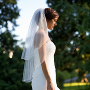 Bride wearing the Elise short sheer wedding veil with a clean finished edge in an outdoor garden setting