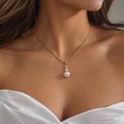 Close-up of the Clara gold-tone pearl pendant necklace worn with a white strapless bridal dress