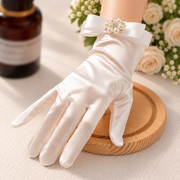 White satin bridal glove with pearl-inspired brooch at the wrist