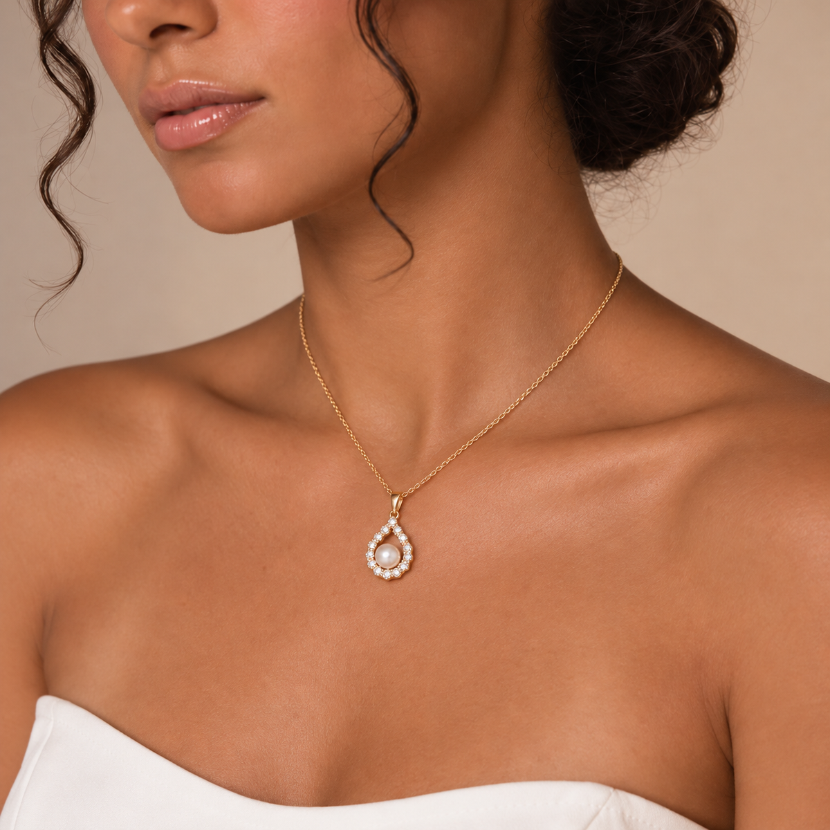 Model wearing the Clara gold-tone necklace with an oval pearl-inspired pendant and an elegant white strapless dress