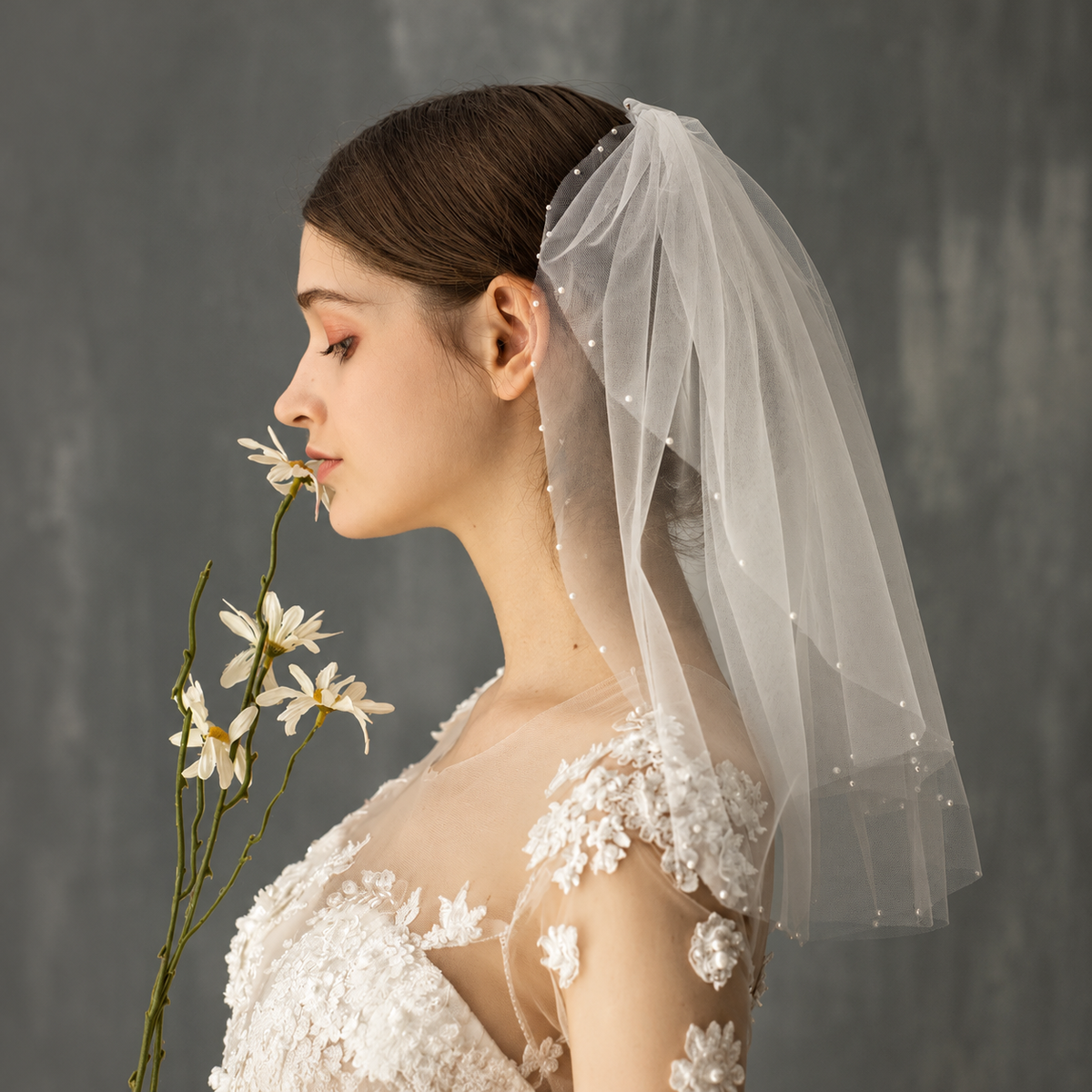 Bride in profile with daisies wearing the Céleste pearl-accented short bridal veil