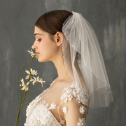 Bride in profile with daisies wearing the Céleste pearl-accented short bridal veil
