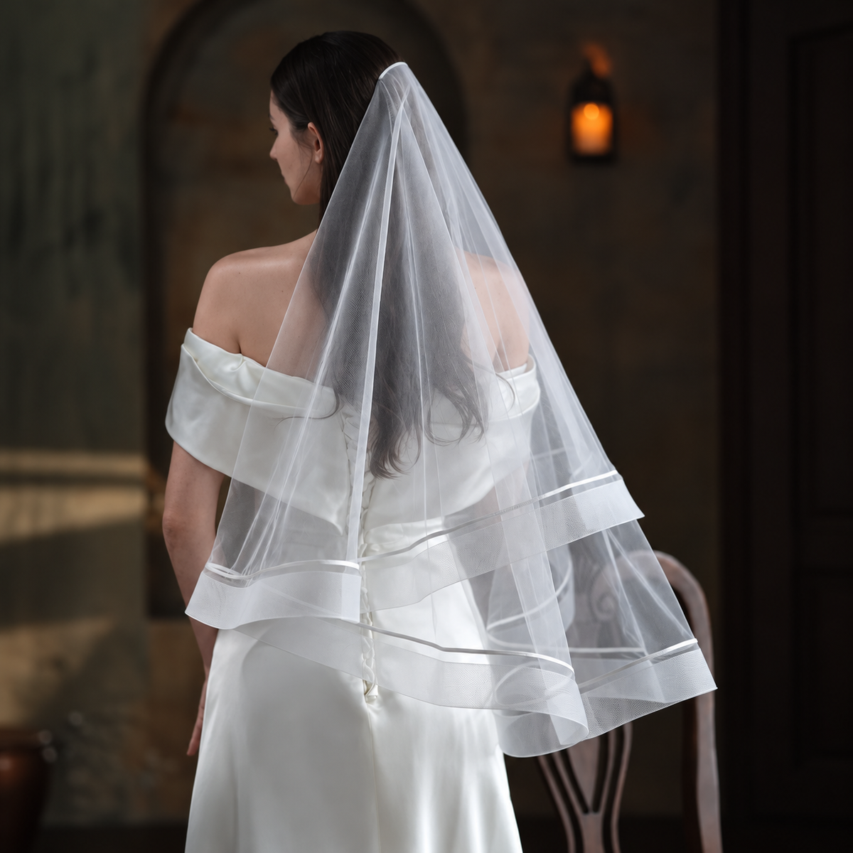 Veiled bride in a candlelit chapel wearing the Celeste satin-trim double-layer veil