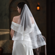 Veiled bride in a candlelit chapel wearing the Celeste satin-trim double-layer veil