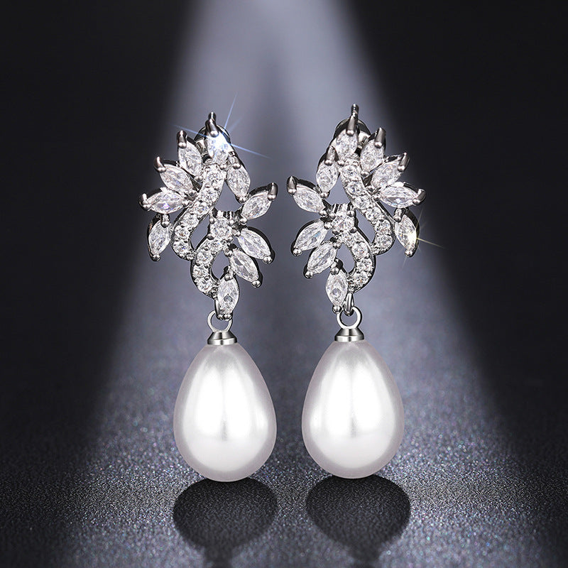 Close-up of Elodie crystal leaf pearl-style earrings against a dark gray background