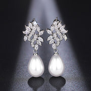 Close-up of Elodie crystal leaf pearl-style earrings against a dark gray background
