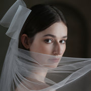 Close-up of a bride wearing the Noelle sheer bow veil with delicate mesh draped across her face