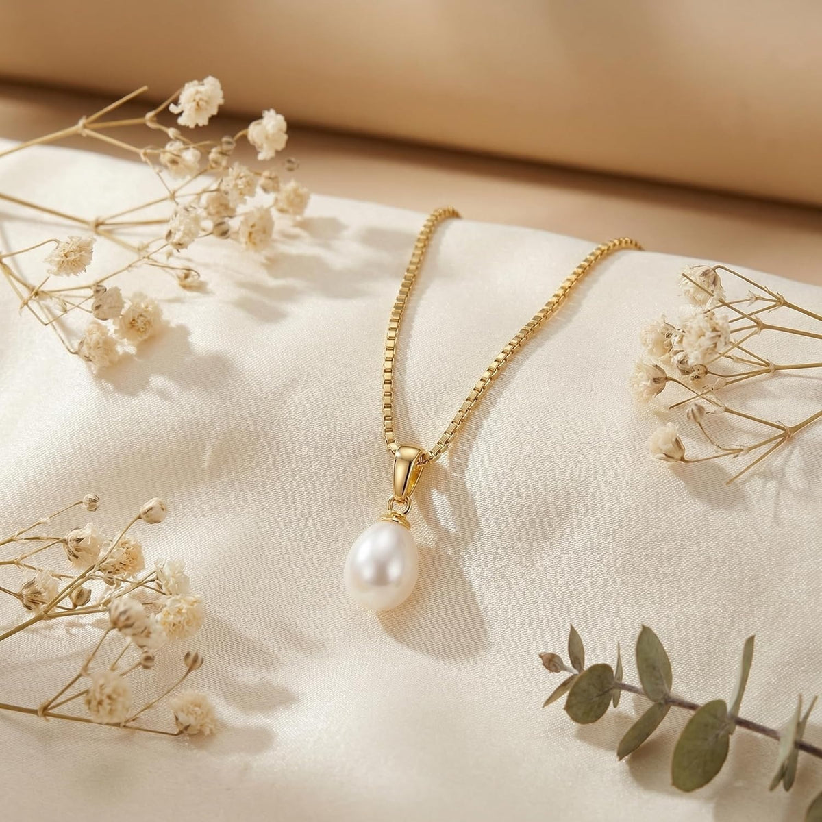 Clara gold-tone pearl pendant necklace displayed on ivory fabric with delicate dried flowers