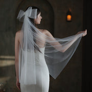 Bride wearing the Noelle sheer bridal veil with an oversized white bow and flowing layered mesh