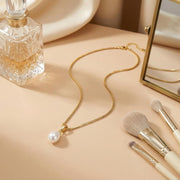 Clara minimalist gold-tone necklace with a white teardrop pearl-inspired pendant on a vanity