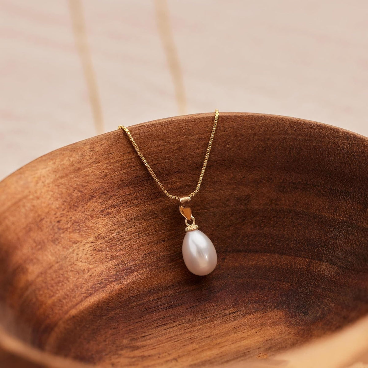Clara pearl drop necklace with a delicate gold-tone chain displayed on a wooden tray
